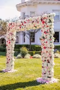 floral wedding arch adorned with white and pink flowers stands on a green lawn