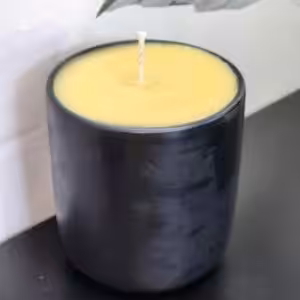 A yellow candle sits in a glossy, dark holder on a black surface