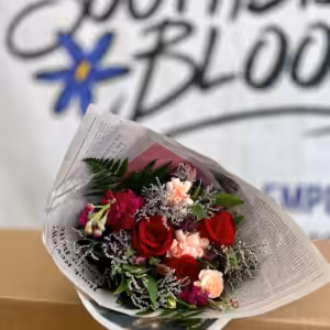 Bouquet of red and pink flowers wrapped in newspaper sits in front of a blurred sign that appears to read South Bloom.