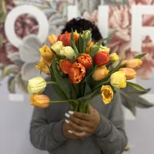 A person holds a vibrant bouquet of tulips in orange, yellow, and red hues.
