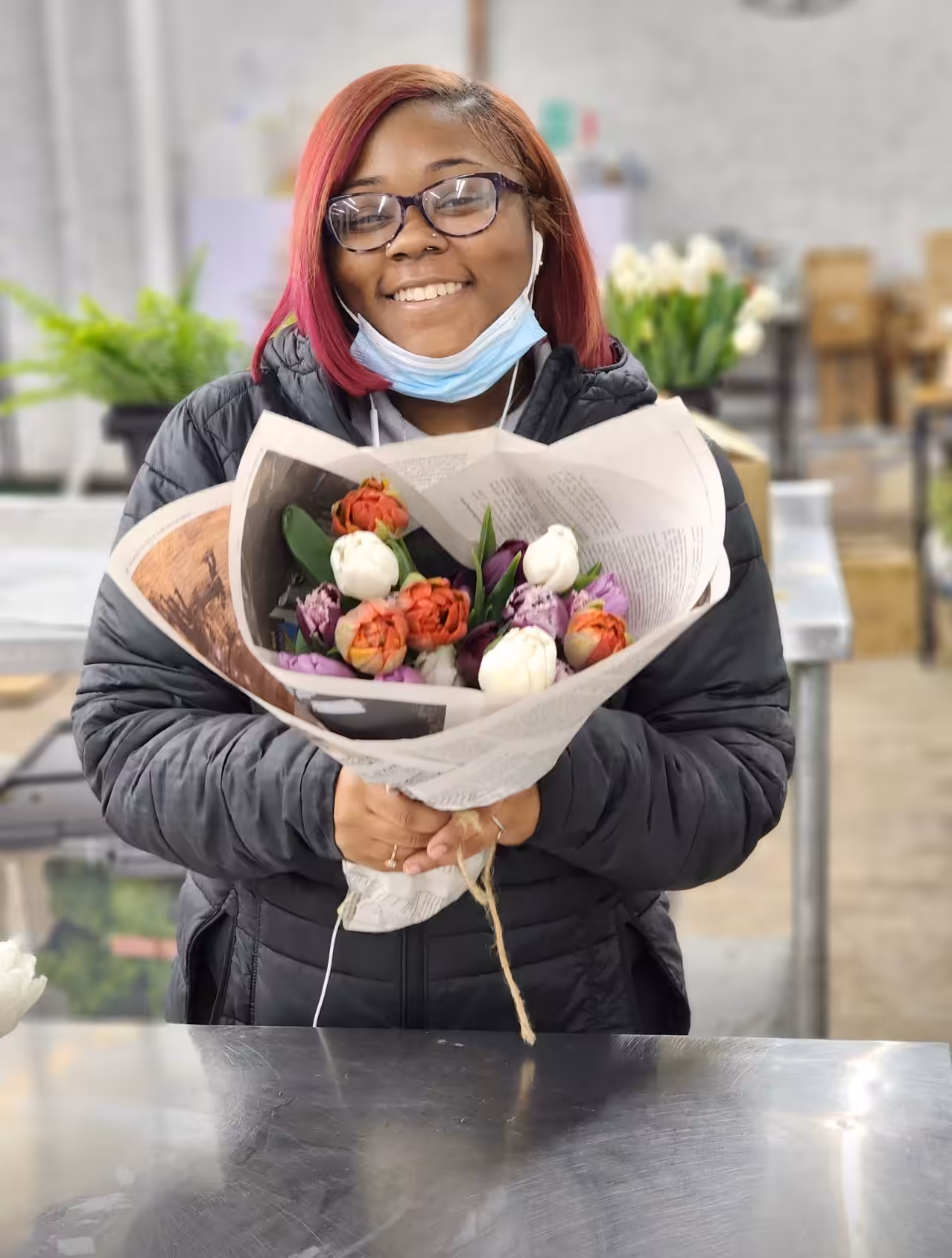Screenshot Smiling Lady with glasses and a black jacket holds a bouquet wrapped in newspaper