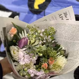 Bouquet of mixed flowers, including lavender, peach, and white blooms, wrapped in newspaper