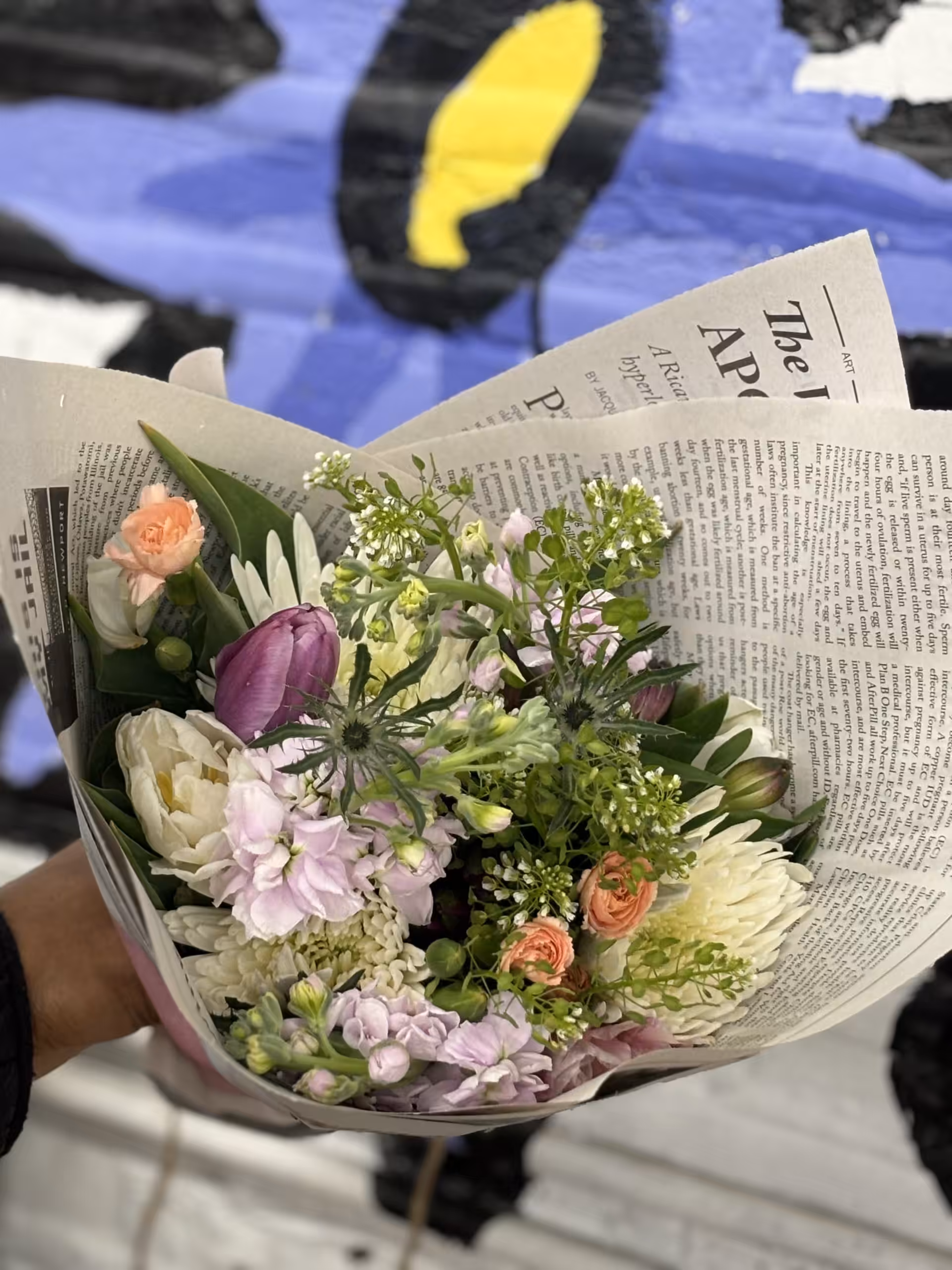 IMG_7445 Bouquet of mixed flowers, including lavender, peach, and white blooms, wrapped in newspaper
