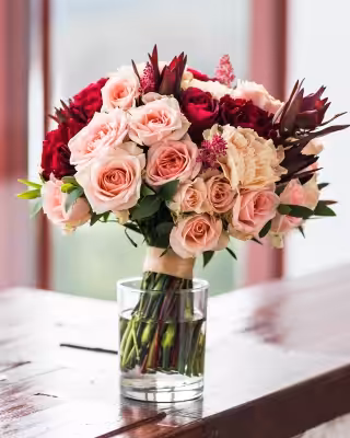 Bouquet of pink and deep red roses in a clear glass vase sits on a wooden table