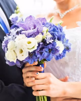 Bride holding a bouquet of vibrant purple and white flowers, standing next to a groom in a dark suit.